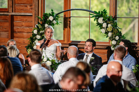 bride gives toast at reception in front of floral arch - 48 Fields Wedding Barn | Northern VA